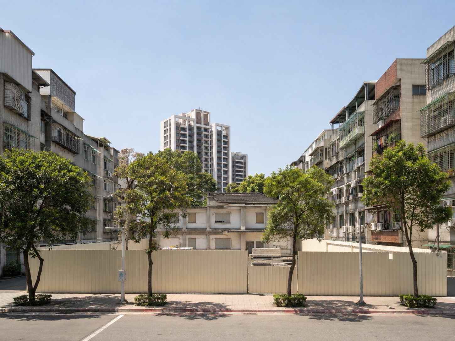 台北市街廓中一塊被施工圍籬圍住的空地,圍籬內是已清空尚未拆除的舊建築,兩側為仍有人居住的老公寓,遠方可見已完工的新建住宅大樓